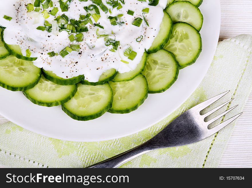 Fresh cucumber slices with sour cream and green onion on a plate