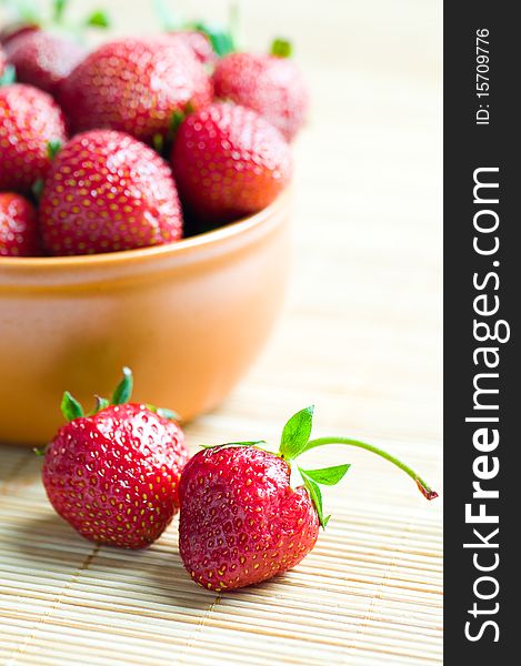 Ripe strawberries in ceramic bowl on wooden background