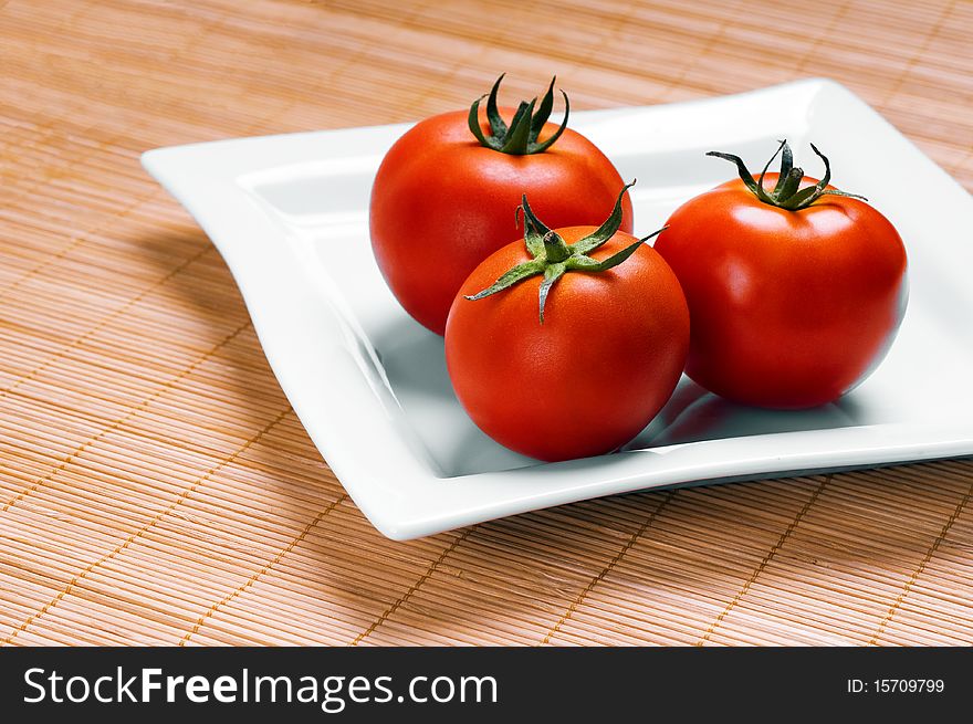 Ripe tomatoes on plate on wooden background