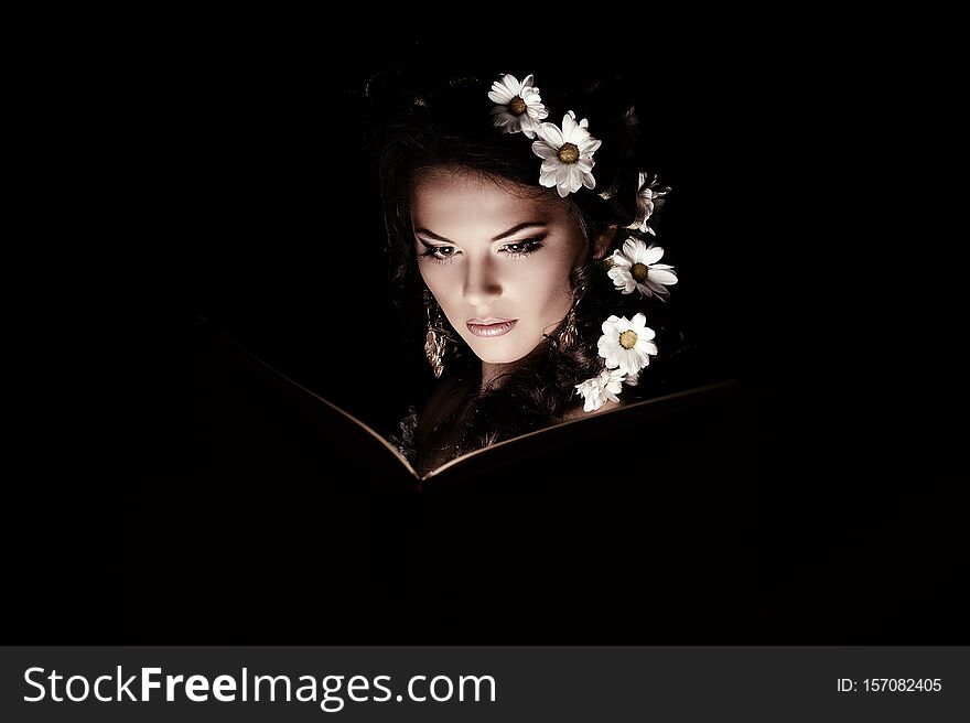 Girl with chamomile reading magic book with mystic light
