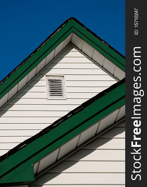 Farmhouse roof peaks with white old white siding and green trim against a deep blue sky. Farmhouse roof peaks with white old white siding and green trim against a deep blue sky.