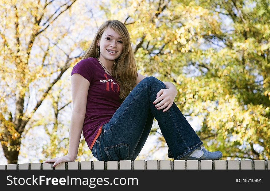 Teenage girl sitting on a white brick wall in early Fall. Teenage girl sitting on a white brick wall in early Fall