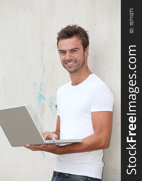 Young man standing against a wall with laptop computer. Young man standing against a wall with laptop computer