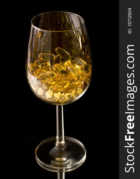 Capsules of lecithin in the wine glass isolated on black. Capsules of lecithin in the wine glass isolated on black