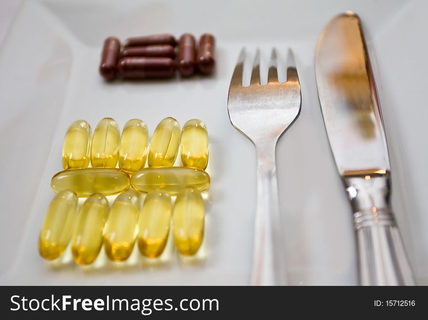 Capsules of lecithin and iron on the white plate with the fork and knife. Capsules of lecithin and iron on the white plate with the fork and knife