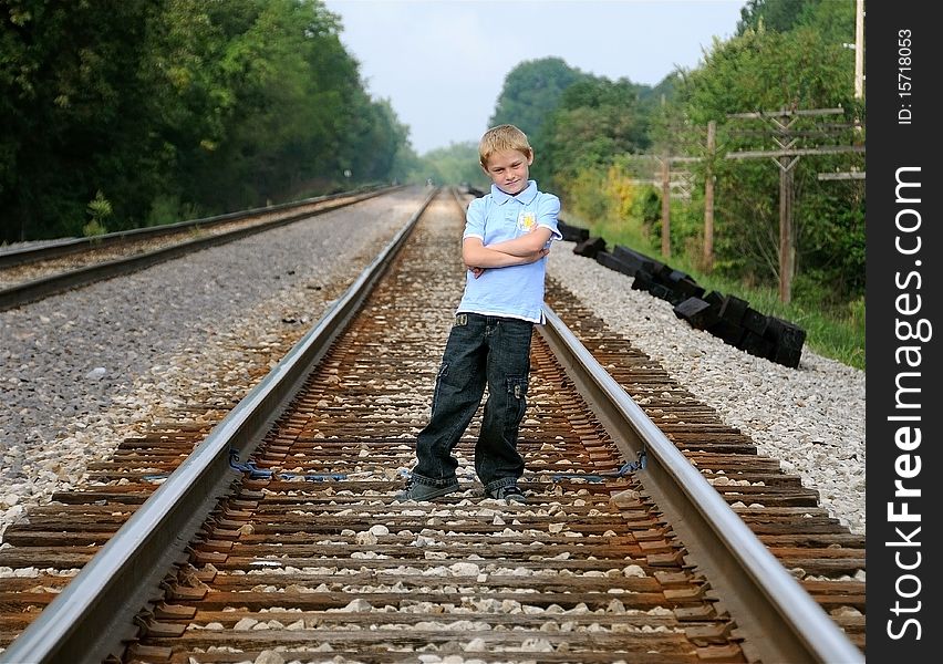 A cute young boy stands on railroad tracks to pose for a photograph.