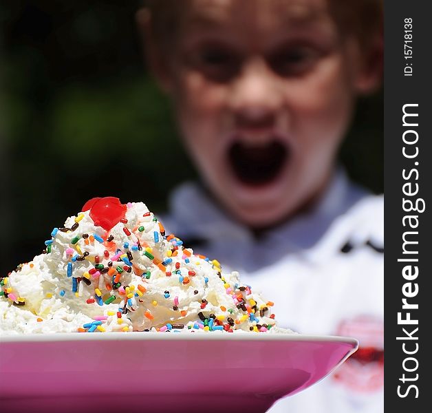 A cute young boy has a surprised, happy look on his face as he looks at a large bowl of ice cream.