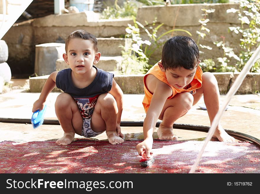 Two little boys are washing the red carpet in the yard. Two little boys are washing the red carpet in the yard
