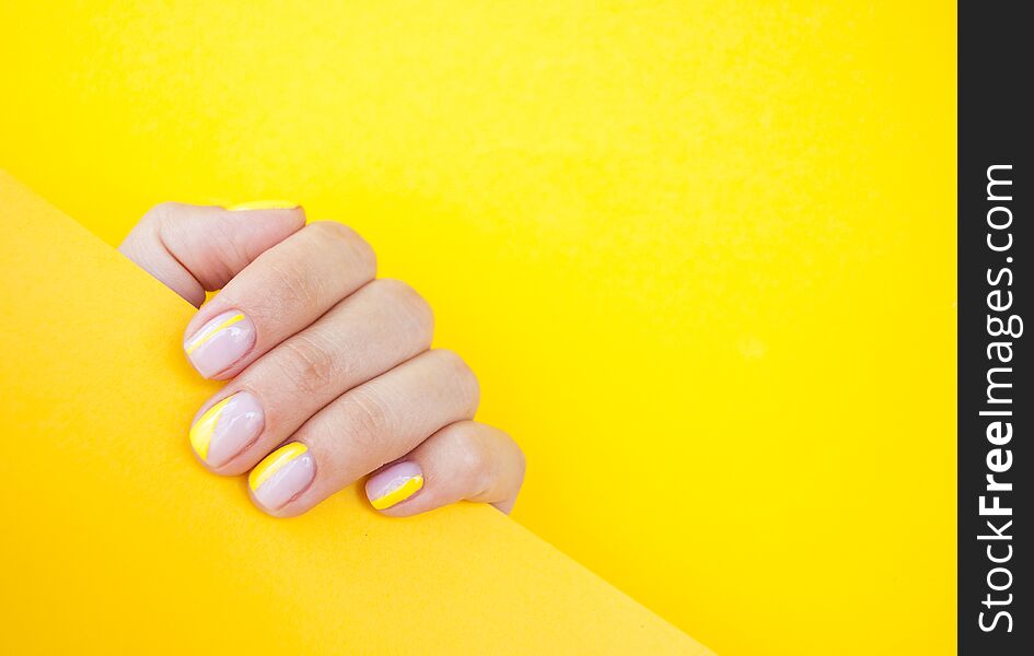 Young woman`s hand with beautiful manicure on yellow color background holding bright yellow paper. Young woman`s hand with beautiful manicure on yellow color background holding bright yellow paper