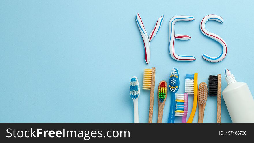 Word YES from toothpaste. Tube of colored toothpaste and toothbrush on blue background. The concept of proper cleaning
