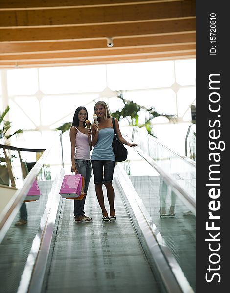 Beautiful teenage girls on escalator at shopping center, eating ice-cream