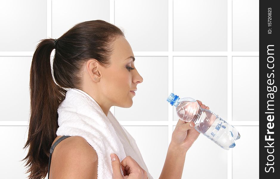 A young and sporty female is drinking water after training. The image is taken on a light gray abstrack background.