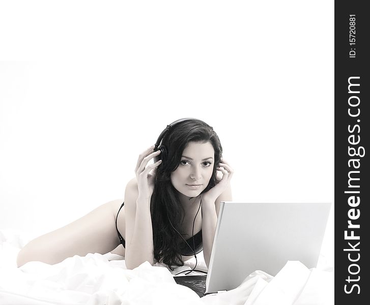 A young and sexy brunette is listening to the music while lying on a white silk blanket. The image is low saturated and isolated on a white background. A young and sexy brunette is listening to the music while lying on a white silk blanket. The image is low saturated and isolated on a white background.