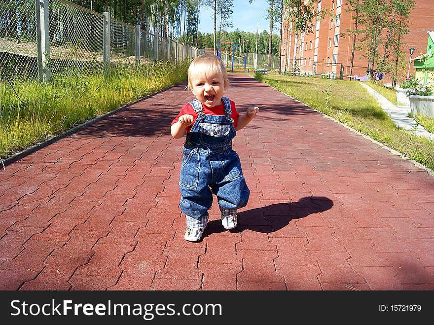 In the summer on a children's athletic field the small smiling child runs on a path. In the summer on a children's athletic field the small smiling child runs on a path