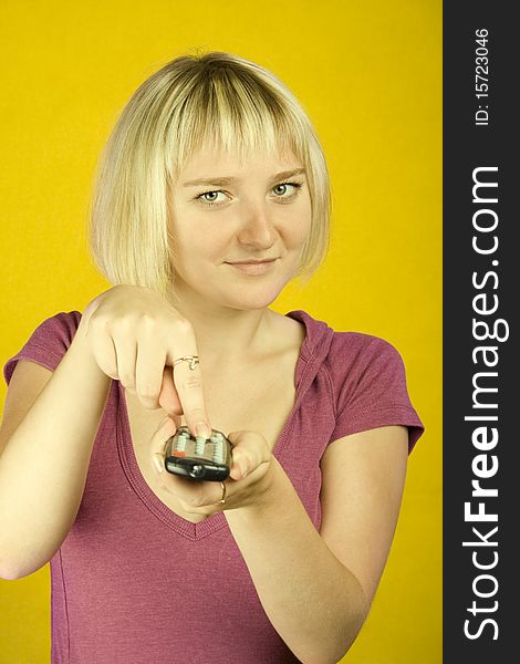 Young woman on yellow background holding a remote control designed into the frame. Finger on the other hand presses the button. Young woman on yellow background holding a remote control designed into the frame. Finger on the other hand presses the button.
