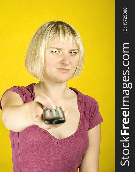 Young woman on yellow background holding a remote control designed into the frame. Finger on the other hand presses the button. Young woman on yellow background holding a remote control designed into the frame. Finger on the other hand presses the button.