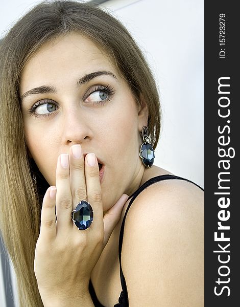 Portrait of elegantly beautiful young woman covers her mouth with his hand. The girl beautiful jewelry, ring and earrings with large blue stones. Portrait of elegantly beautiful young woman covers her mouth with his hand. The girl beautiful jewelry, ring and earrings with large blue stones