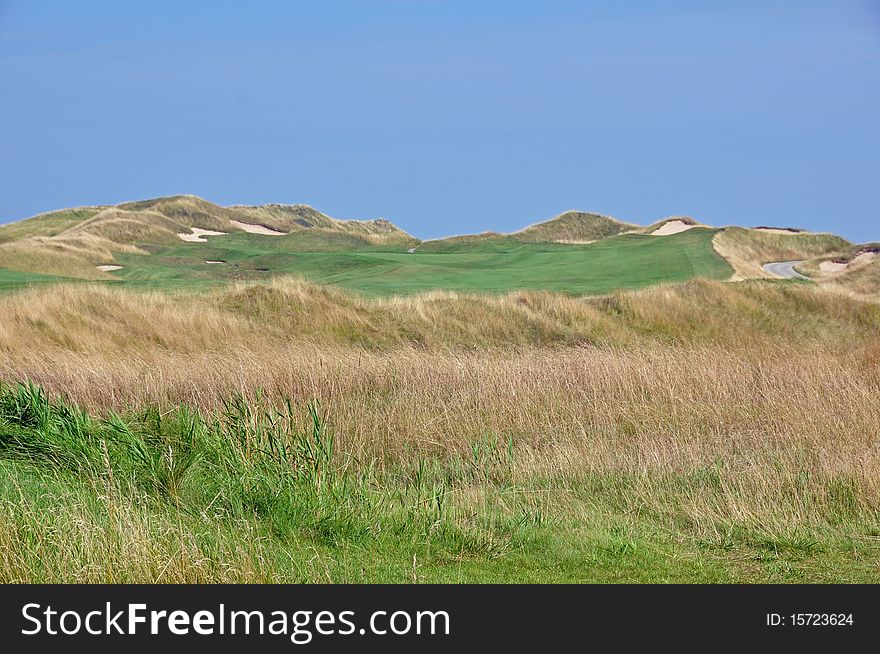 A golf course fairy surrounded by high grass and dune style bunkers. A golf course fairy surrounded by high grass and dune style bunkers