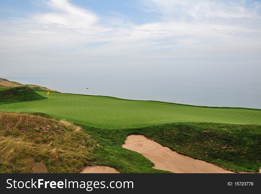 A golf green on a cliff over a body of water. A golf green on a cliff over a body of water