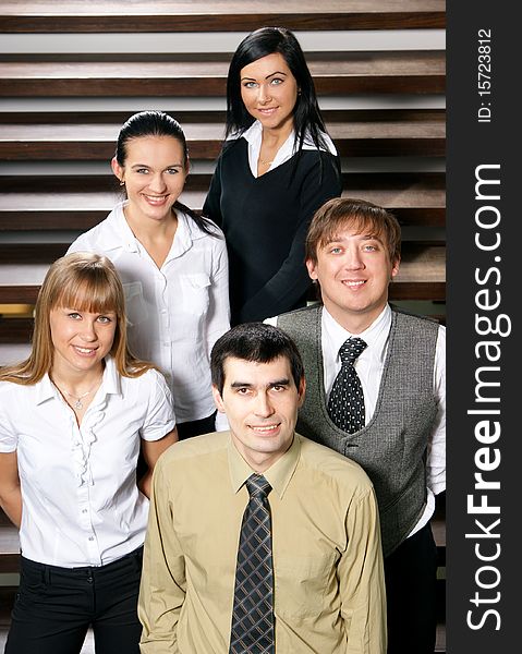 Five young business persons are standing as a team with a man in front. The image is taken on a background with stairs. Five young business persons are standing as a team with a man in front. The image is taken on a background with stairs.