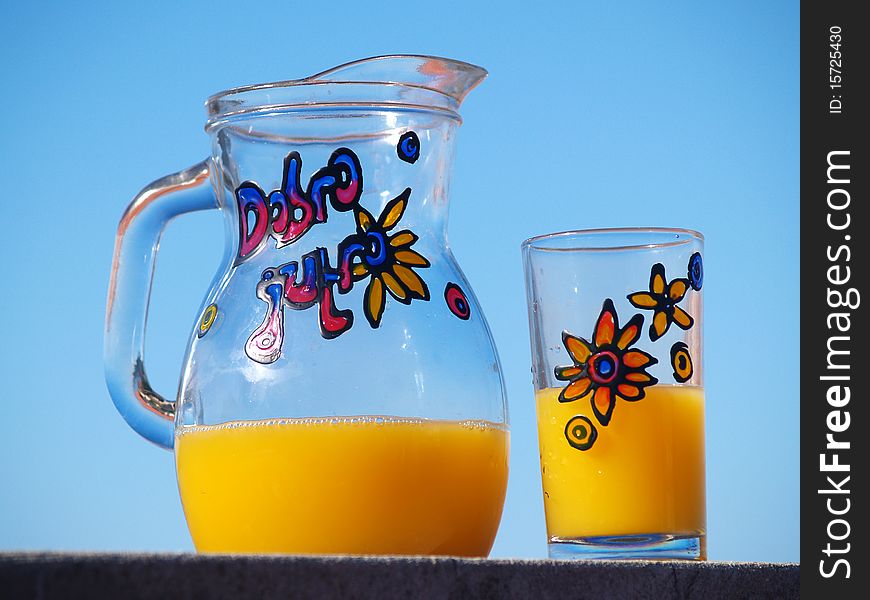 Jar and glass with orange juice, blue sky at the background. Jar and glass with orange juice, blue sky at the background