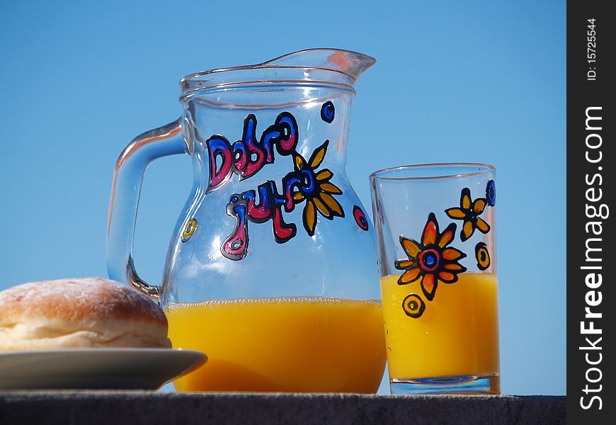 Jar and glass filled with orange juice and doughnut, blue sky at the background. Jar and glass filled with orange juice and doughnut, blue sky at the background