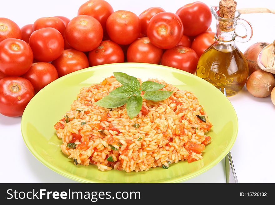 Risotto with tomatoes on a green plate decorated with basil with fresh tomatoes, onions, garlic and olive oil on white background