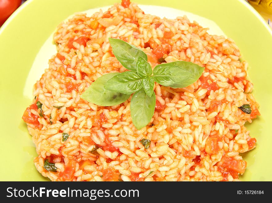 Risotto with tomatoes on a green plate decorated with basil in close up