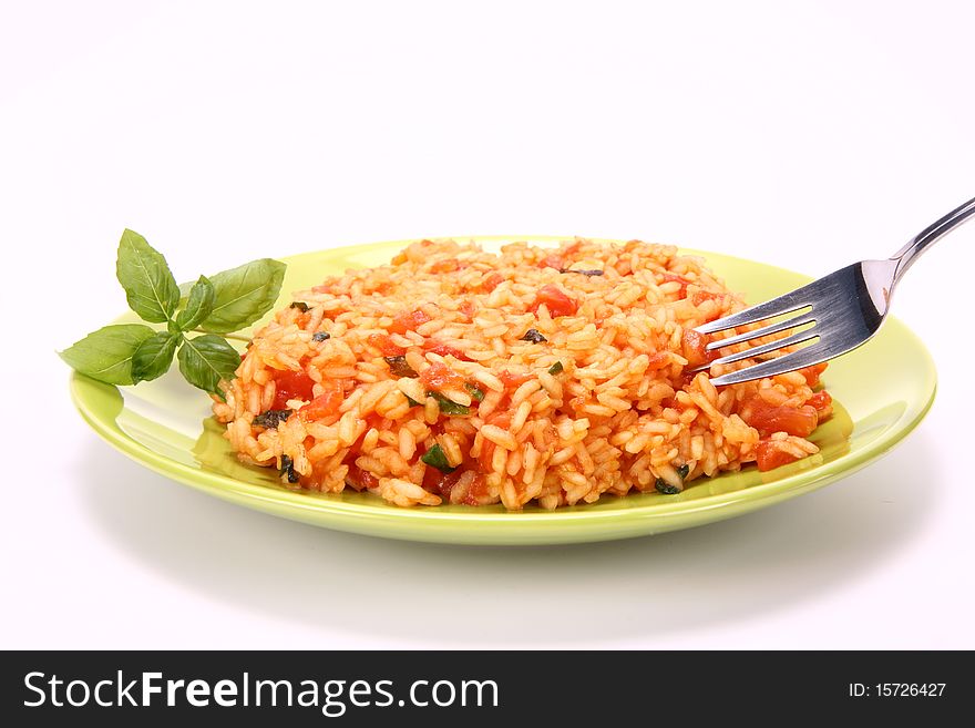 Risotto with tomatoes on a green plate decorated with basil being eaten with a fork