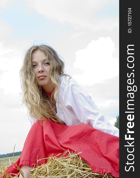 Woman with long hair in red clothes sits in the summer on straw. Woman with long hair in red clothes sits in the summer on straw