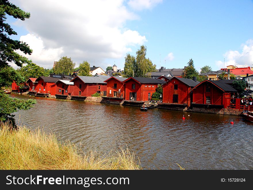 A tipical landscape in Finland in the city of Porvoo, with red houses rounded by trees and t heblue and cloudy sky in the background.