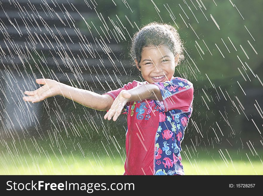 Little girl holding out both her hands to feel water while it is being sprinkled around her, smiling. Little girl holding out both her hands to feel water while it is being sprinkled around her, smiling