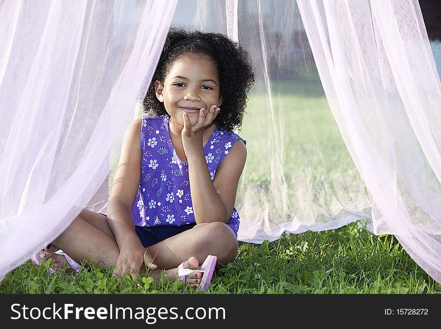 Little girl sitting in the grass under/in a canopy with her head in her hands. Little girl sitting in the grass under/in a canopy with her head in her hands