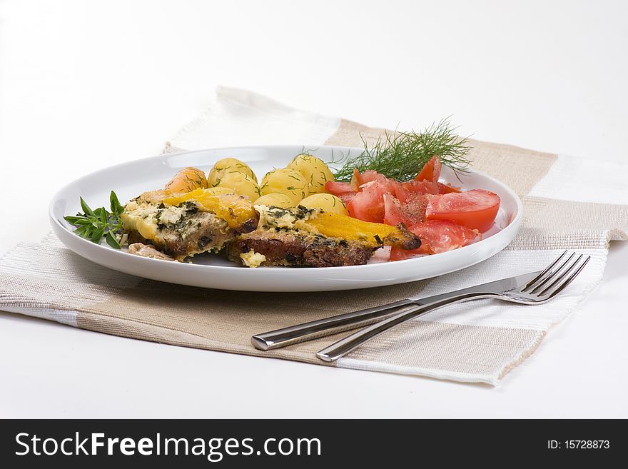 Roast pork, potatoes, tomatoes and basil on a plate