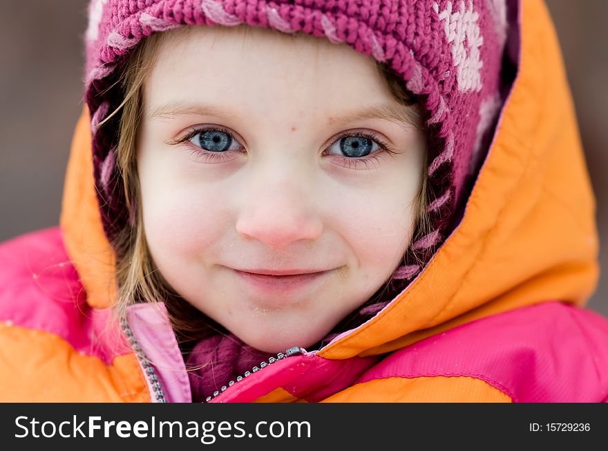 Nice toddler girl with blue eyes in winter pink hat looking into the camera. Nice toddler girl with blue eyes in winter pink hat looking into the camera