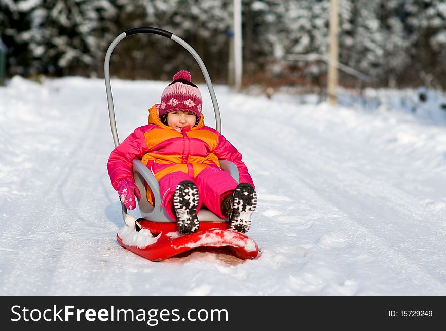 Nice toddler girl with blue eyes in winter pink hat sitting on sleighand looking into the camera. Nice toddler girl with blue eyes in winter pink hat sitting on sleighand looking into the camera