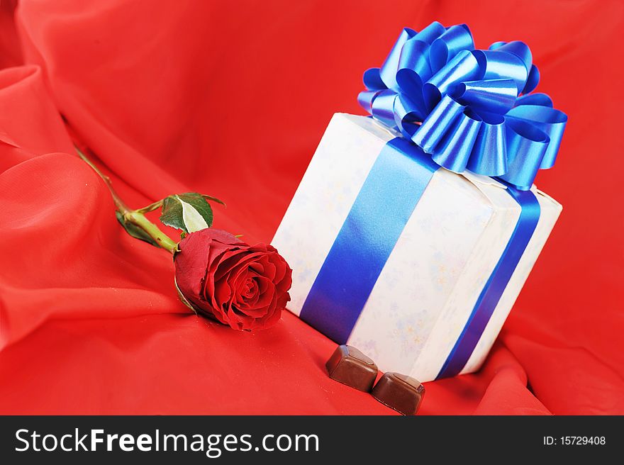 Beautiful red rose, gift and chocolate on red close up