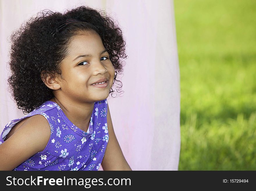 Little girl sitting in front of light pink canopy with her head facing 3/4 towards you. Little girl sitting in front of light pink canopy with her head facing 3/4 towards you
