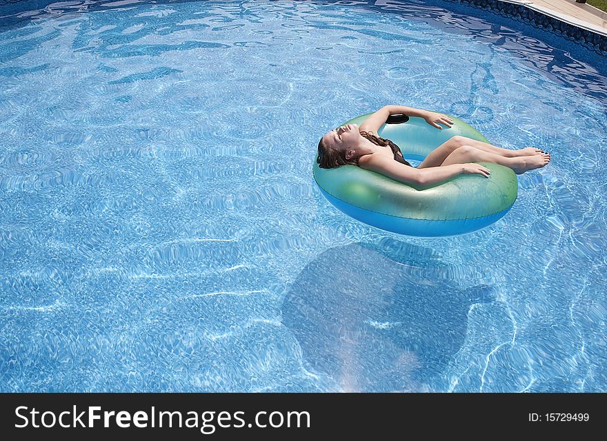Teenage girl floating in pool on a green tube