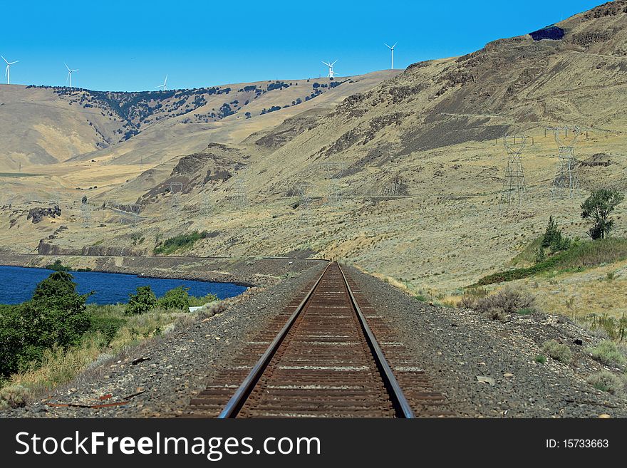 Train tracks in Oregon, next To the Columbia River with wind mills and Electric towers as a background. Train tracks in Oregon, next To the Columbia River with wind mills and Electric towers as a background