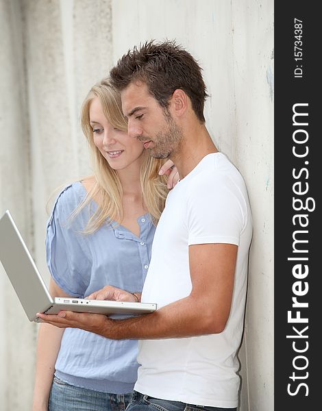 Couple standing against a wall with laptop computer. Couple standing against a wall with laptop computer