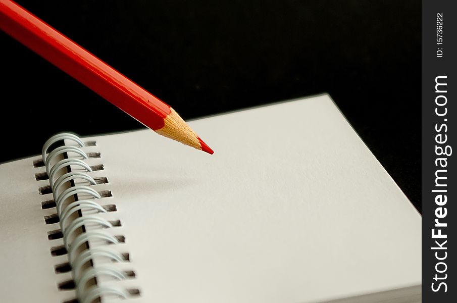 Red pencil with notebook in black background