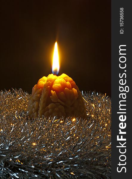 Christmas candle with flame nestled in a bed of silver tinsel on a black background. Christmas candle with flame nestled in a bed of silver tinsel on a black background