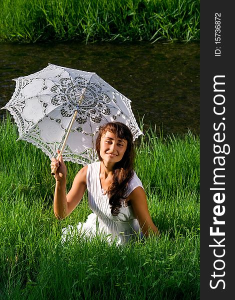 Young  attractive girl in white with sun umbrella sitting in the fresh green grass near the river. Young  attractive girl in white with sun umbrella sitting in the fresh green grass near the river