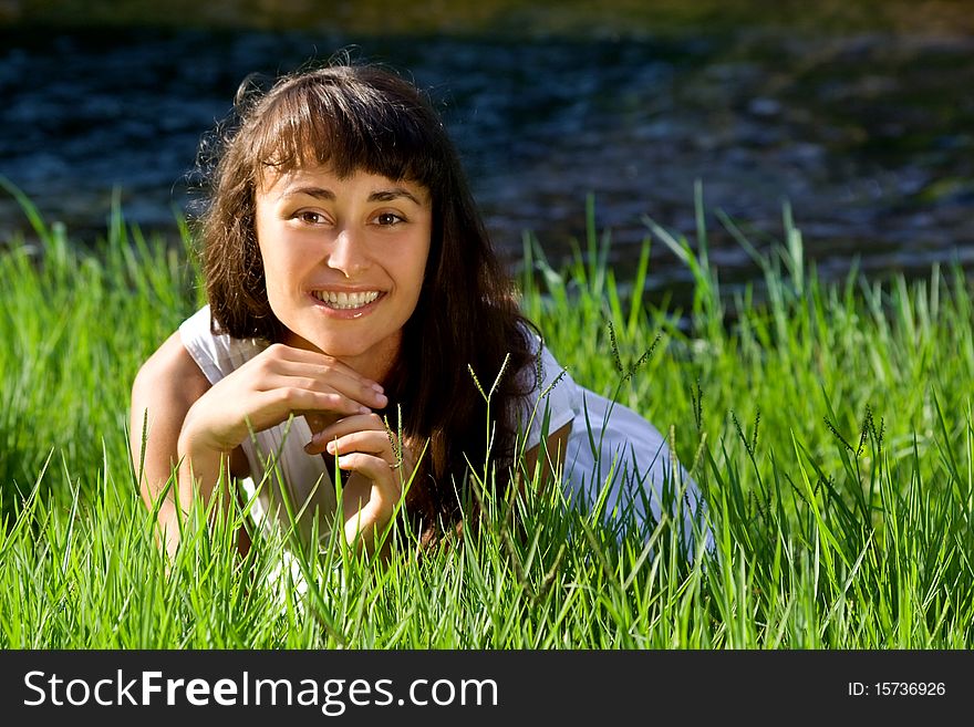 Beautiful young girl liying on green grass near the blue stream. Beautiful young girl liying on green grass near the blue stream