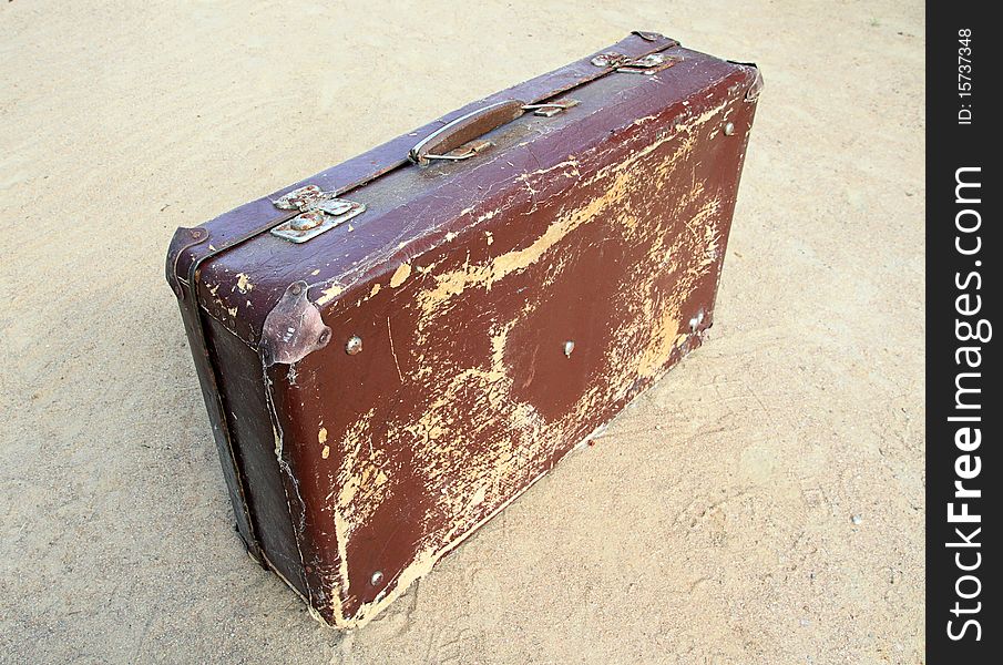 Old valise on yellow sand