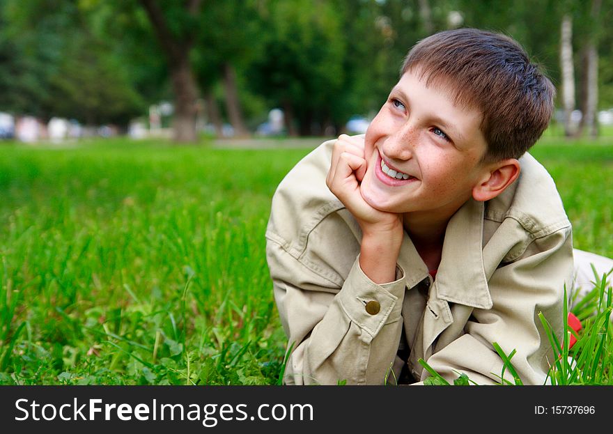 Young beautiful happy boy lays on a grass