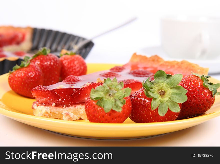 Piece of Strawberry Tart on a yellow plate decorated with strawberries with a cup of coffee and a tart pan in the background