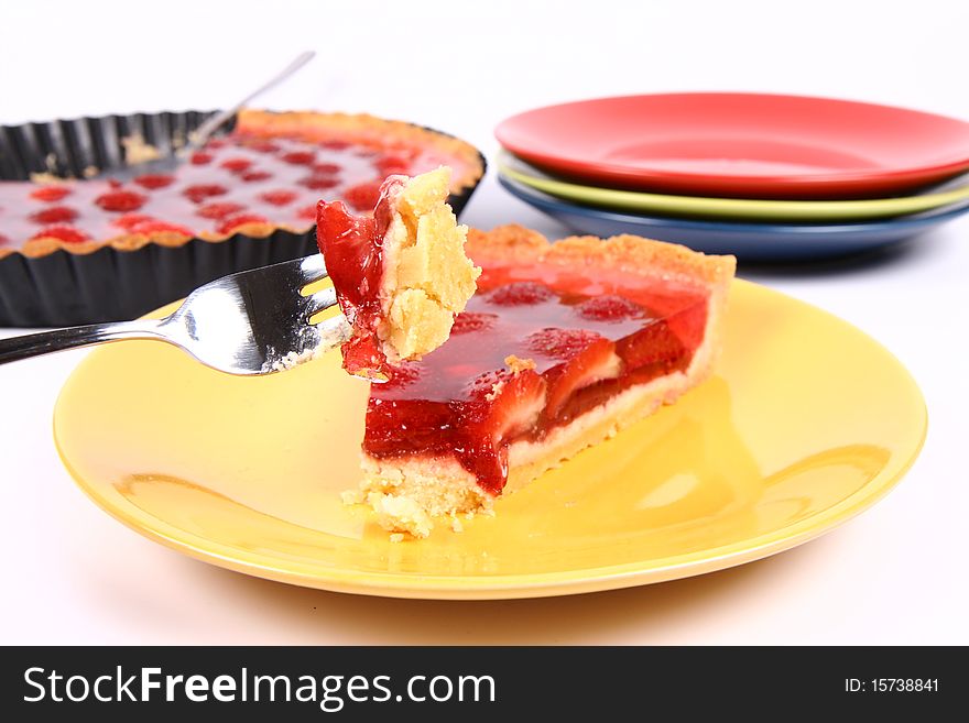 Piece of Strawberry Tart on a yellow plate a tart panand plates in the background and some of the tart on a fork