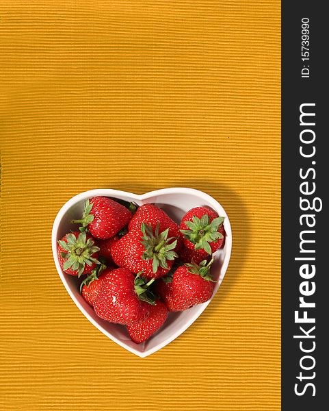 Strawberries in a heart shaped bowl on a yellow canvas background